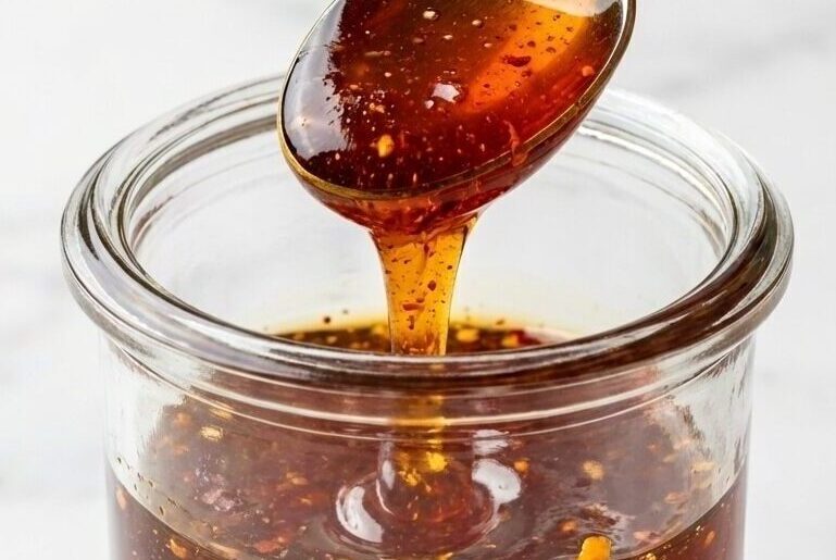 Clear honey being poured through a fine-mesh strainer to ensure a smooth texture for this hot honey recipe.