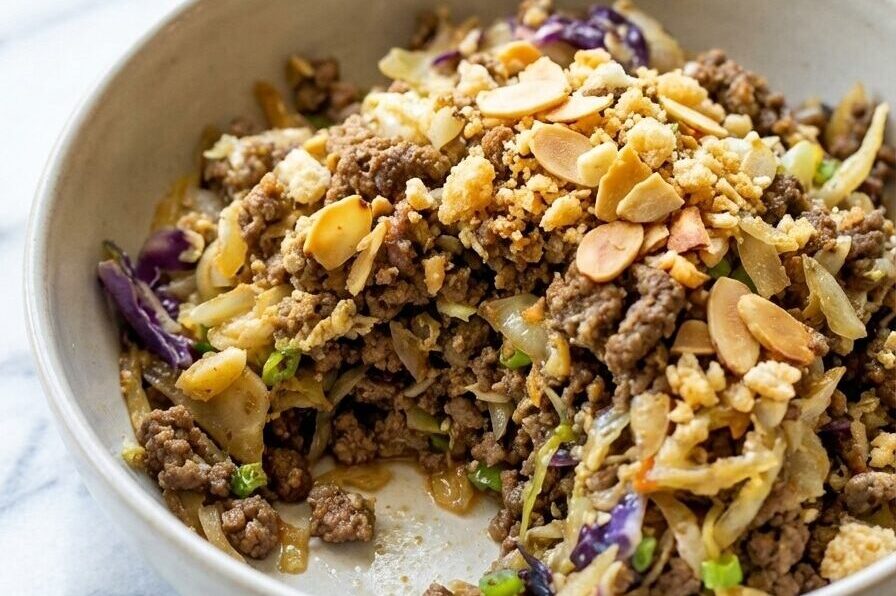 Keto egg roll in a bowl topped with a crispy toasted almond and pork rind crumble in a dark ceramic dish.