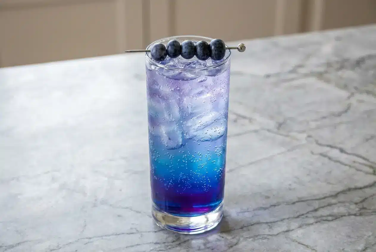 A tall glass of a vibrant homemade blue raspberry energy drink recipe, made with natural syrup and garnished with a lemon wheel.